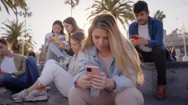 Ung Blond Flicka Sitter Koncentrerad Skriva Mobil Med Grupp Vänner — Stockvideo
