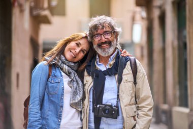 Portrait Caucasian smiling mature tourist love couple posing for photo outdoors. Happy adult people romantic embraced. Man and woman looking at camera together affectionately enjoying weekend getaway. clipart