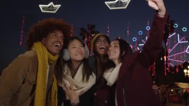 Selfie videolu telefon çok ırklı grup gülen meslektaşları kışın eğleniyorlar. Genç gülümseyen nesiller birlikte heyecanlanan insanlar topluluğun tadını çıkarıyorlar. Akşamları lunaparktaki arkadaşların şaşırmış yüzleri.