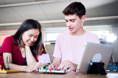 Teknik liseden beyaz bir oğlan ve Asyalı bir kız teknoloji sınıfındaki bir robotik tahtaya bakıyorlar. Üniversite arkadaşları fizik elektroniği çalışıyor. Laboratuvarda elektrikli robotları programlayan insanlar.