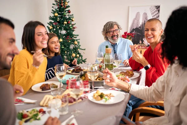 Laughing family gathering celebrating Christmas meal together at festive table. People having fun and eating together at home on Thanksgiving Day. Three Caucasian generations enjoying domestic life.