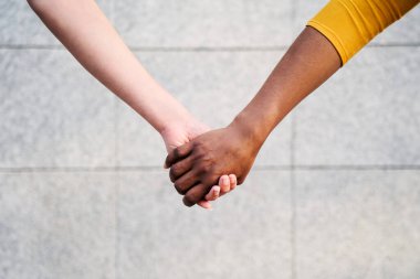 Çok ırklı iki kadının el ele tutuşmasını yakından takip edin. Açık havada farklı genç lezbiyen çiftler. İnsanlar arasında homoseksüel ilişkiler. Reklam için arkaplanı ve alanı kopyala.