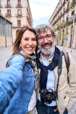 Dikey özçekim gülümseyen olgun Kafkasyalı turist çift dışarıda poz veriyor. Grimsi erkek ve yetişkin kadın sevgi dolu kucaklaşmalar. 60 'lı yıllarda aşık olan mutlu insanlar birlikte kameraya bakıp şehrin tadını çıkarıyorlar..