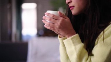 Genç ve güzel Asyalı kadın oturma odasında gözleri kapalı bir fincan çay ya da kahve içiyor. Evde oturan sakin bekar kadın. Sıradan Çinli insanlar rahat bir ifadeyle sıcak içeceğin tadını çıkarıyor..