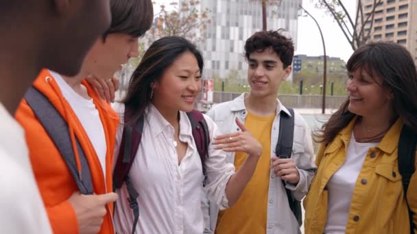 一群年轻的多文化学生看着笑着的亚洲女孩 聚集人们站在室外享受课余时间 中国女人对朋友们说着动听的话 回学校去 — 图库视频影像