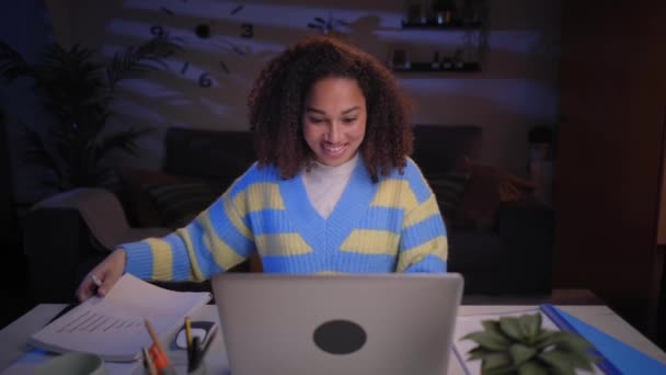 年轻的拉丁微笑的女人晚上在家里用笔记本电脑 快乐的女孩看着电脑 快乐的人坐在客厅的办公桌前 电子通勤和努力工作的概念 — 图库视频影像
