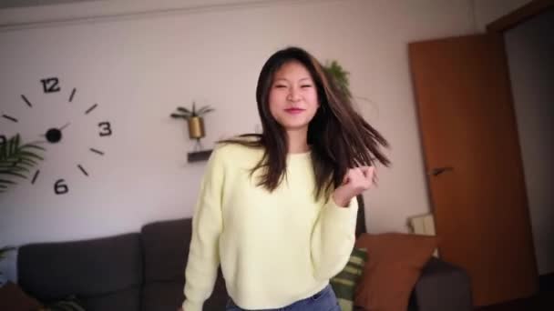 魅力的なアジアの少女はリビングルームで一人で踊るのが楽しいです エキサイティングな中国の女性インフルエンサーは ソーシャルメディアのためのウイルスダンスの動きを行います シングル世代Zの人々は自宅で自由な時間を楽しんでいます — ストック動画