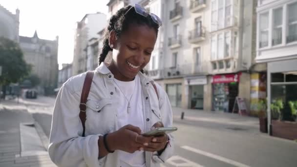 Piękna Młoda Czarna Kobieta Spacerując Ulicą Komórką Rękach Wygląda Uśmiechnięta — Wideo stockowe