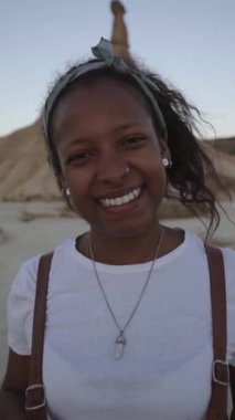 Dikey Portreli neşeli genç seyahat eden kadın çöl bardenalarında günbatımının tadını çıkarıyor. Afro-Amerikalı kız dışarıda kameraya bakarak mutlu mesut duruyor. İnsanlar ıssız bölgelerde tatildeler..