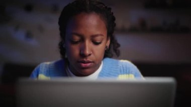Akşamları evde dizüstü bilgisayar kullanarak konsantre olan genç Afrikalı üniversiteli kıza yaklaş. Ciddi bir kadın gece geç saatlerde bilgisayara bakıyor. Z kuşağı öğrenci rakip ve işçi kavramı. 