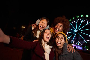 Selfie telefonları kışın eğlenen çok ırklı meslektaşlar grubu. Genç gülümseyen nesiller birlikte heyecanlanan insanlar topluluğun tadını çıkarıyorlar. Akşamları lunaparktaki arkadaşların şaşırmış yüzleri.. 