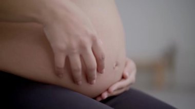 Spor giyim giymiş, yoga pozu veren, tanınmayan hamile, beyaz kadın. Beyaz kadın kocaman karnına dokunuyor. Bebek bekleyen fitness insanları. Odaklanmamış arkaplan.