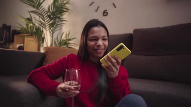 Latin Amerikalı kadın, evde rahat ve mutlu bir şekilde beyaz şarap içerken telefonla iletişim kuruyor ve sesli mesajlar alıyor. Genç kız evde tek başına vakit geçiriyor.