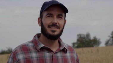 Gülümseyen tarım mühendisi kameraya bakıyor. Tarım endüstrisi teknisyeninin portresi. Şapkalı beyaz erkek, kırsal kesimde günlük giysiler, kırsal kesimde tarlalar.