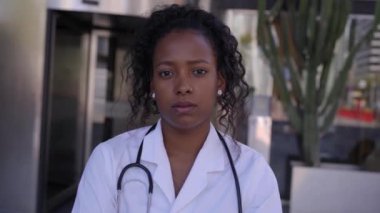 Genç Latin doktor kameraya ciddi bir hareketle bakıyor. Hastanenin dışındaki kadın sağlık uzmanı. Afrikalı Amerikalı kadın sağlık çalışanı endişeli görünüyor. Özel acil bakım görevlileri.