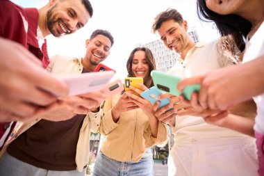 Bir grup genç açık havada cep telefonu kullanıyor. Neşeli arkadaşlar renkli cep telefonlarına bakıp sosyal ağlarda eğleniyorlar. Z jenerasyonu, teknolojiye bağımlılık