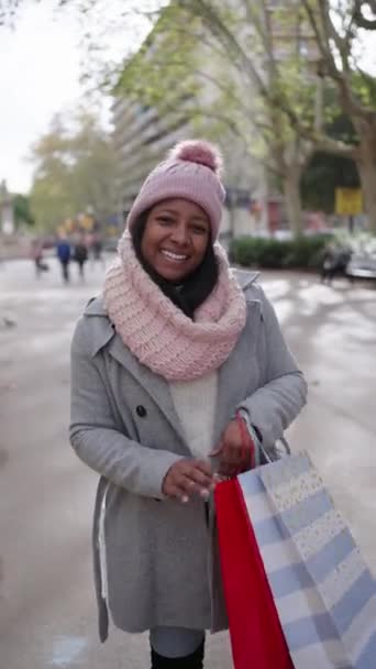 垂直录像 身着冬衣的年轻拉蒂娜女人在镜头前展示了几袋圣诞礼物 在城市街上度假的快乐的非洲裔美国女孩享受着微笑的假期 — 图库视频影像