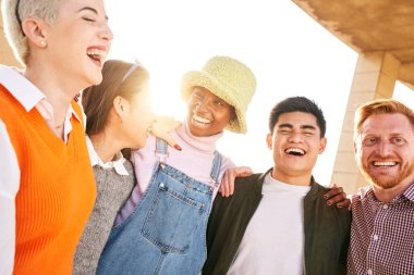 Kucaklaşan çok ırklı bir grup öğrenci çok gülüyor. Gün batımında üniversitenin dışında gülüyorlar. Birlikte eğlenen genç insanlar topluluğu. Sosyal toplanma ve gençlik kültürü kavramı