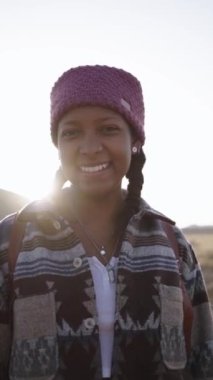 Dikey portre, gülümseyen genç sırt çantalı örgüler çölde güneşli bir günün tadını çıkarıyor. Güzel Afro-Amerikalı kadın, dışarıda kameraya bakarken mutlu mesut duruyor. Issız bölgelerde tatil yapan insanlar..