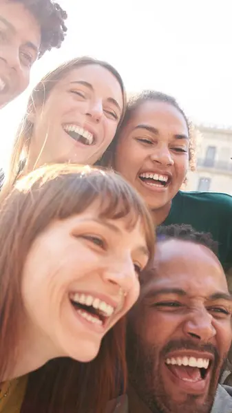 Happy smiling multi-ethnic group friends having fun together. Multiracial diverse young colleagues embracing posing for selfie photo on street in city. Multicultural friendship generation Z concept.