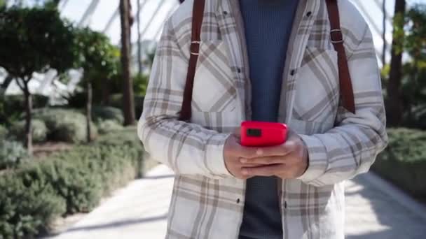 一个无法辨认的年轻人用手机在城市公园里行走的正面镜头 在阳光明媚的冬日户外散步时 专注于男性在手机上打字的双手 与网络相连的人 — 图库视频影像