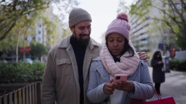 这对年轻貌美的情侣通过手机坠入爱河 在城市街道上欢度寒假 一边走一边拥抱 一边提着礼品袋庆祝圣诞节 — 图库视频影像
