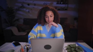 Genç Latin kadın gece evde not defterine not alarak konsantre oluyor. Afro kız işe dizüstü bilgisayarla odaklanmış. Üniversite öğrencisi oturma odasında masada oturuyor. Uzaktan çalışan genç bir kadın.