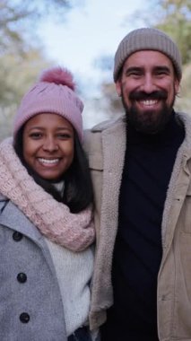 Çok ırklı, güzel bir çiftin dikey portresi. Açık havada yaşayan genç bir kadın ve aşık bir adam kameraya bakıp gülümsüyor. Noel zamanı arka planda. İnsanlar kış kıyafetleri giyiyordu.