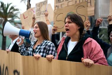 İklim değişikliği ve küresel ısınma gösterilerinde konuşan ve megafonla protesto eden kızgın ve asi bir kadın. Bir grup aktivist, dünya yanlısı pankartlarla ortaya çıktı.