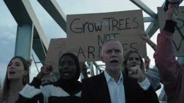 Dünyadaki savaş ve şiddete karşı gösteri yapan çok ırklı bir grup. İnsanlar ağaç yetiştirmek için yazılı pankartlarla toplandı. Ordu ve savaş karşıtı değil.