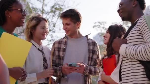 多種多様な世代のZの若い笑顔のグループは 彼らが手に持っているスマートフォンで面白いビデオを喜んで見ています モバイルセル屋外でソーシャルビデオゲームを使用して一緒に楽しんでいる友人 — ストック動画