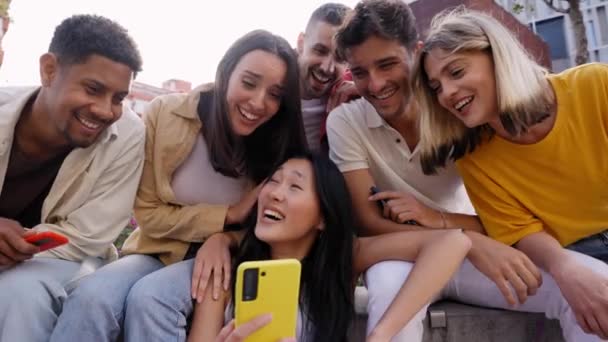 一群年轻人在电话里笑着看东西 多种族朋友一起坐在户外用手机 社交网络和新一代科技成瘾的概念 — 图库视频影像