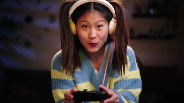 专注的亚洲女人晚上一个人坐在客厅里玩电子游戏 中国女人们带着耳机庆祝胜利 一代Z和甜蜜的家 — 图库视频影像