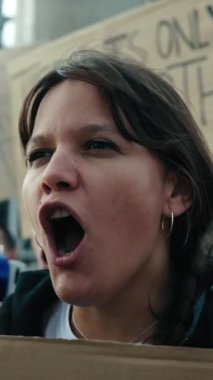 Dikey. Küresel ısınma iklim değişikliği gösterisinde konuşan ve megafonla protesto eden kızgın ve asi bir kadın. Dünya yanlısı bir grup aktivist pankartlarla ortaya çıktı.