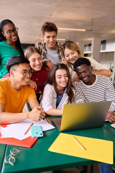 Dikey geniş bir grup genç çok ırklı öğrenci sınıfta gülümseyerek toplandı ve dizüstü bilgisayardan komik bir şey izleyerek eğlendiler. Z jenerasyonu arkadaşları içerideki ekran bilgisayarını kullanarak ve arayarak