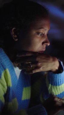 Dikey Kenar Görünümü, evde dizüstü bilgisayar kullanan Latin bir kız. Ciddi bir kadın, oturma odasında masasında oturan bilgisayarlara bakıyor ve daktilo yazıyor. Aygıt ekranı ile aydınlatılmış kadın insanlar