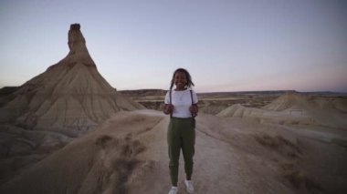 Genç Afrikalı Amerikalı kadın, kırsal kesimde gün batımında kameraya bakıp gülümsüyor. Doğadaki neşeli kız yaz tatilinin tadını çıkarıyor. Güzel bir bayan gezgin. Bardenas Çölü Gerçekleri