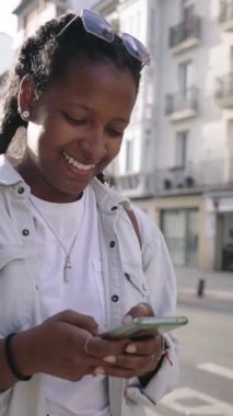 Dikey. Elinde cep telefonuyla caddede yürüyen güzel siyah bir kadın telefon ekranında gülüyor ve komik görünüyor. Sohbet ediyor ve ses kayıtlarını şehirde gezdiriyor..