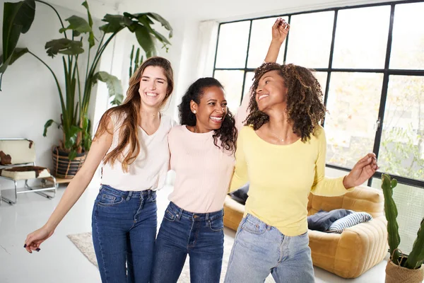 Group of excited attractive multiracial young women celebrating party at home. Beautiful friends enjoying leisure in company dancing hugging indoors. Generation z people and positive relationships.
