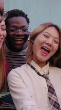 Genç uluslararası üniversite öğrencilerinden oluşan dikey grup, Asyalı bir kızın cep telefonuyla yaptığı komik videoları izlerken mutlu bir şekilde gülümsüyor. Nesil z arkadaşı neşeli fakülte kampüsü dışında cep telefonuna bakıyor
