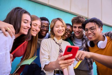 Bir grup genç uluslararası üniversite öğrencisi, Asyalı bir kızın akıllı telefonuyla komik videolar izlerken mutlu bir şekilde gülümsüyor. Nesil z arkadaşları fakülte kampüsünün dışında cep telefonlarına bakıyorlar.