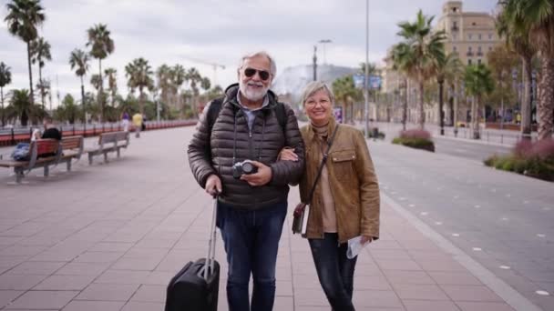 镜头在笑着的白种人成熟的游客夫妇的镜头中放大 他们站在街头摆出一副带着行李的样子 丈夫和妻子穿着冬衣在阳光灿烂的日子享受退休生活 — 图库视频影像