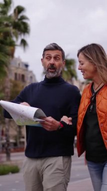 Dikey yetişkin Kafkas turist çifti ellerinde harita tutarak gezip yerleri göstererek konuşuyorlar. Kadın ve erkek, şehir caddesinde mutlu tatilin tadını çıkarıyorlar. Yetişkin turizm insanları 