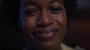 Mutlu gülümseyen genç zenci kadın yüzüne yakın çekim. Afro-Amerikalı kadın kameraya neşeli görünüyor. Geceleri evde pozitif davranışları olan afro bir kız. Bin yıllık neslin doğal güzelliği.