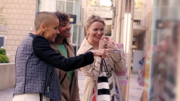 3人の興奮する成熟した女性が街の店の窓に興味を持って見ています 多民族の友人のグループ 屋外ショッピングバッグを保持する喜びの女性 友情関係 セールス バーゲン ショッピング — ストック動画