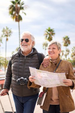 Dikey gülümseyen olgun Kafkasyalı turist çifti bavulları yana bakan kaygısızca sarılıyorlar. Mutlu karı koca kış güneşli bir günde dışarıda emeklilik tatilinin tadını çıkarıyorlar.