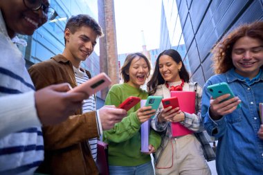 Bir grup genç açık havada cep telefonu kullanıyor. Neşeli arkadaşlar renkli cep telefonlarına bakıp sosyal ağlarda eğleniyorlar. Z jenerasyonu, teknolojiye bağımlılık