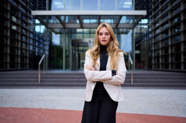 Şık bir yetişkin işi takım elbiseli güzel sarışın kadın şirket ofisinde duruyor. Güçlü beyaz kadın, kendine güvenen poz veriyor. Dışarıdaki kameraya ciddi bakıyor. Alan inşa arkaplanını kopyala