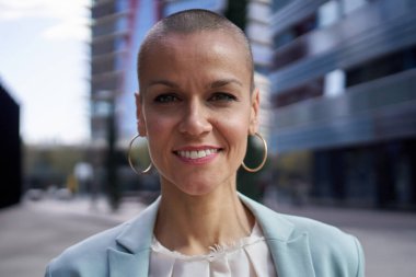 Kameraya gülümseyen orta yaşlı beyaz iş kadınının yakın plan portresi. Neşeli, çekici bir bayan dışarıda mutlu poz veriyor. Tıraş olmuş, beyaz, pozitif ifadeli.