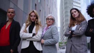 Düşük açılı hareketli kadın girişimciler şehirdeki güçlü kadın işlerinden takım elbiseliler. Farklı ırktan ve yaşlardan beş ciddi iş arkadaşı dışarıda kollarını kavuşturmuş kameraya güveniyorlar.